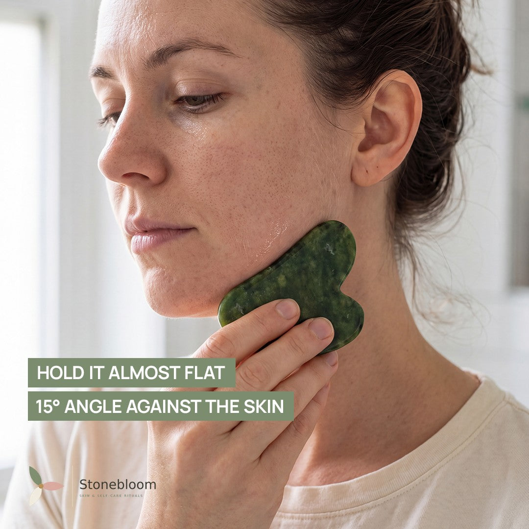 Woman holding the jade gua sha stone almost flat against her jawline at a 15 degree angle